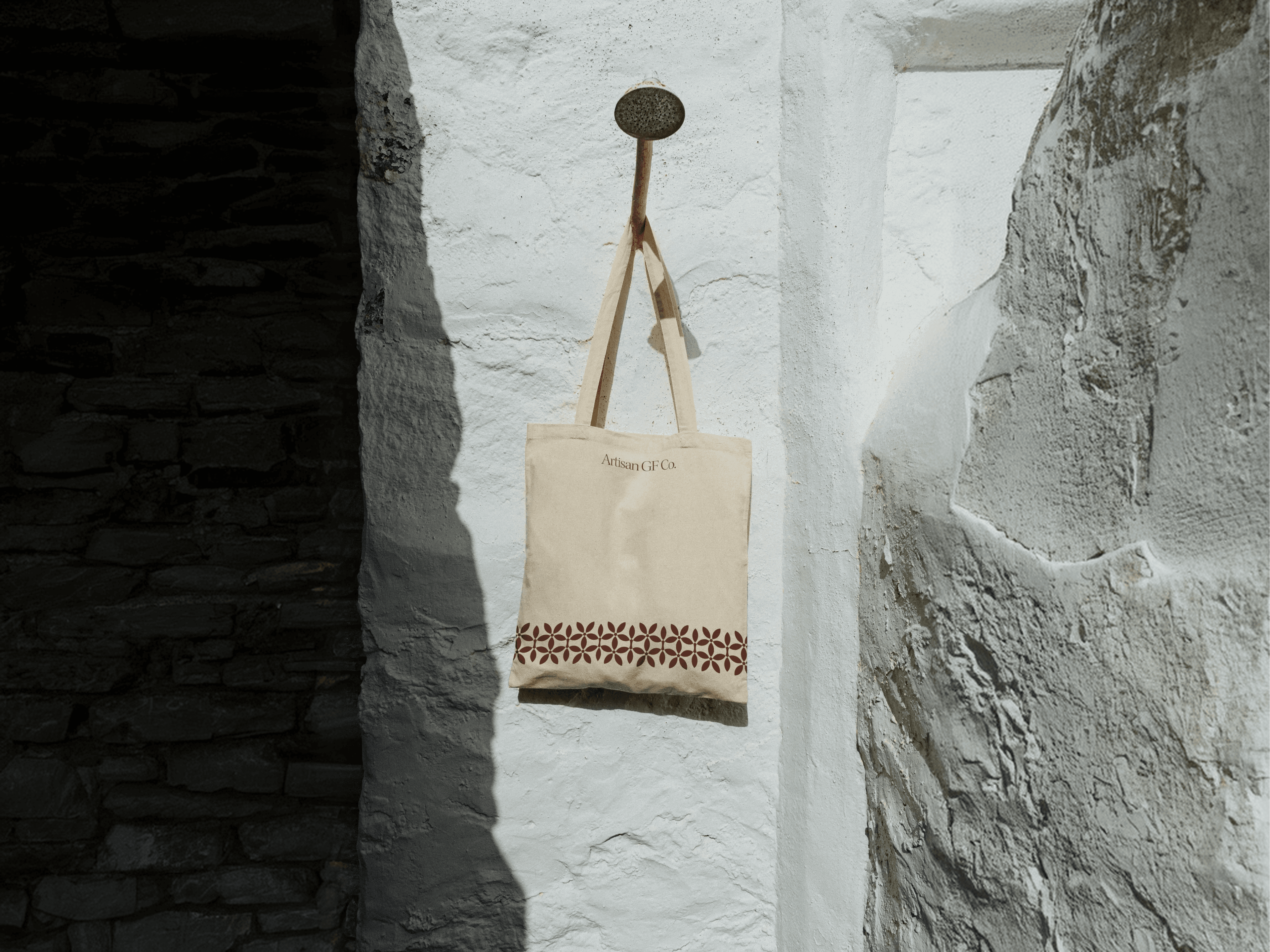 Artisan GF Co. cream tote bag with a berry cyclamen border, hanging against a whitewashed stone wall