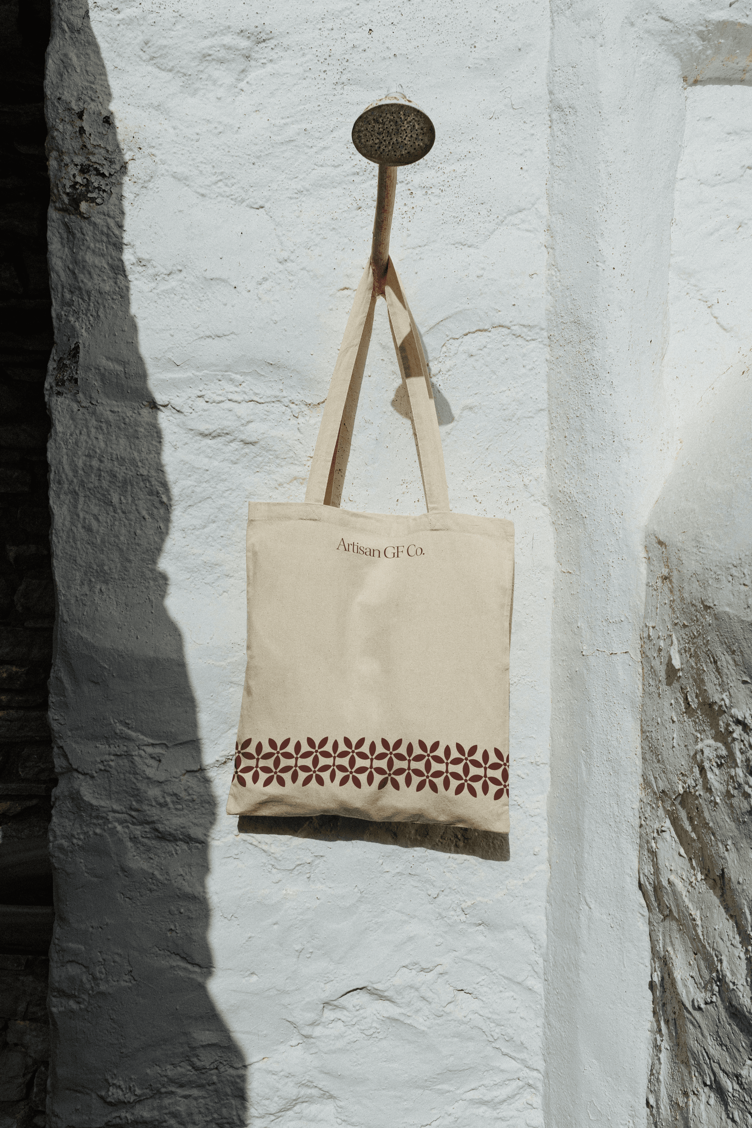 Artisan GF Co. cream tote bag with a berry cyclamen border, hanging against a whitewashed stone wall