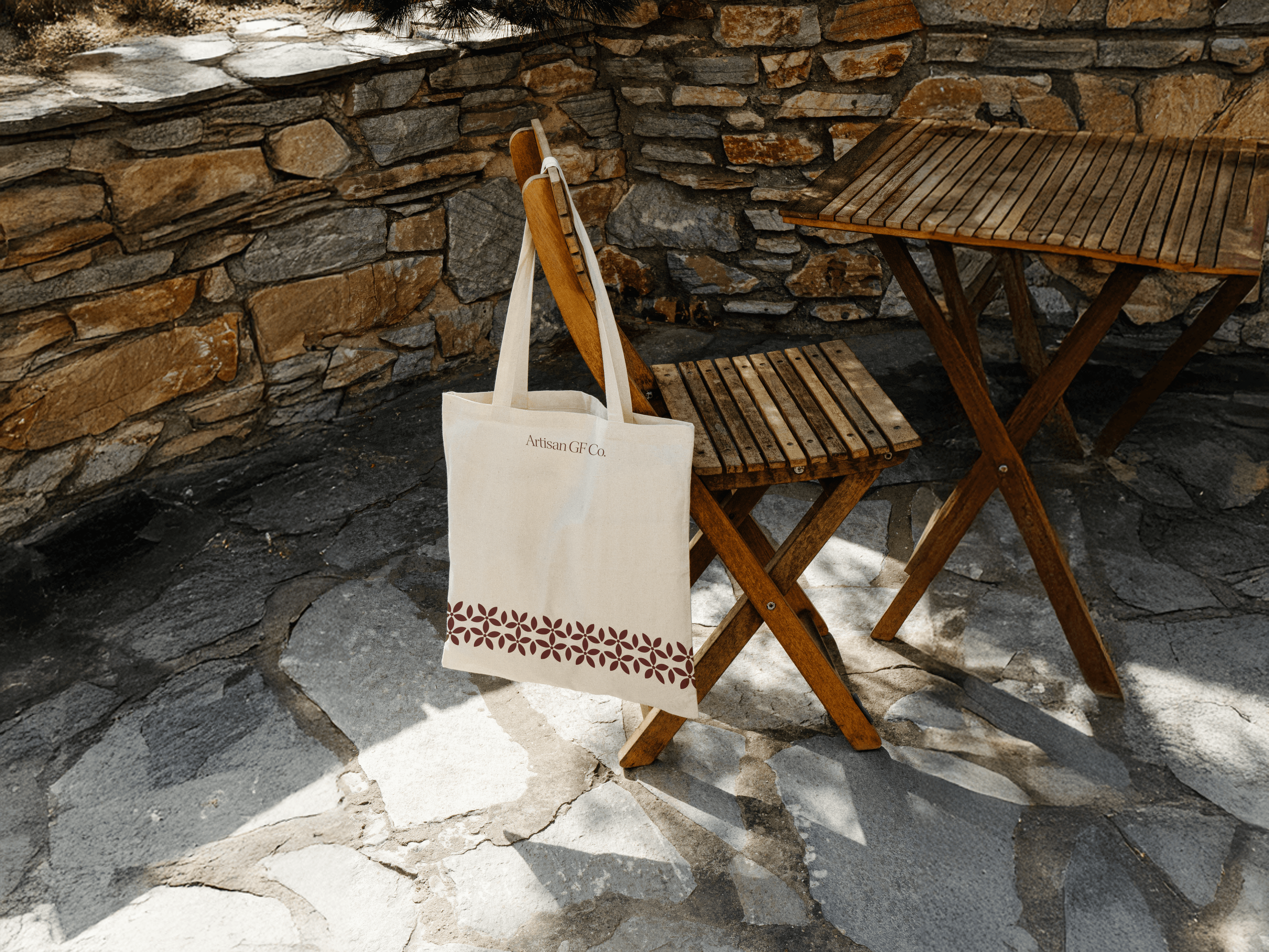 Artisan GF Co. tote bag hanging from a timber chair against a stone wall