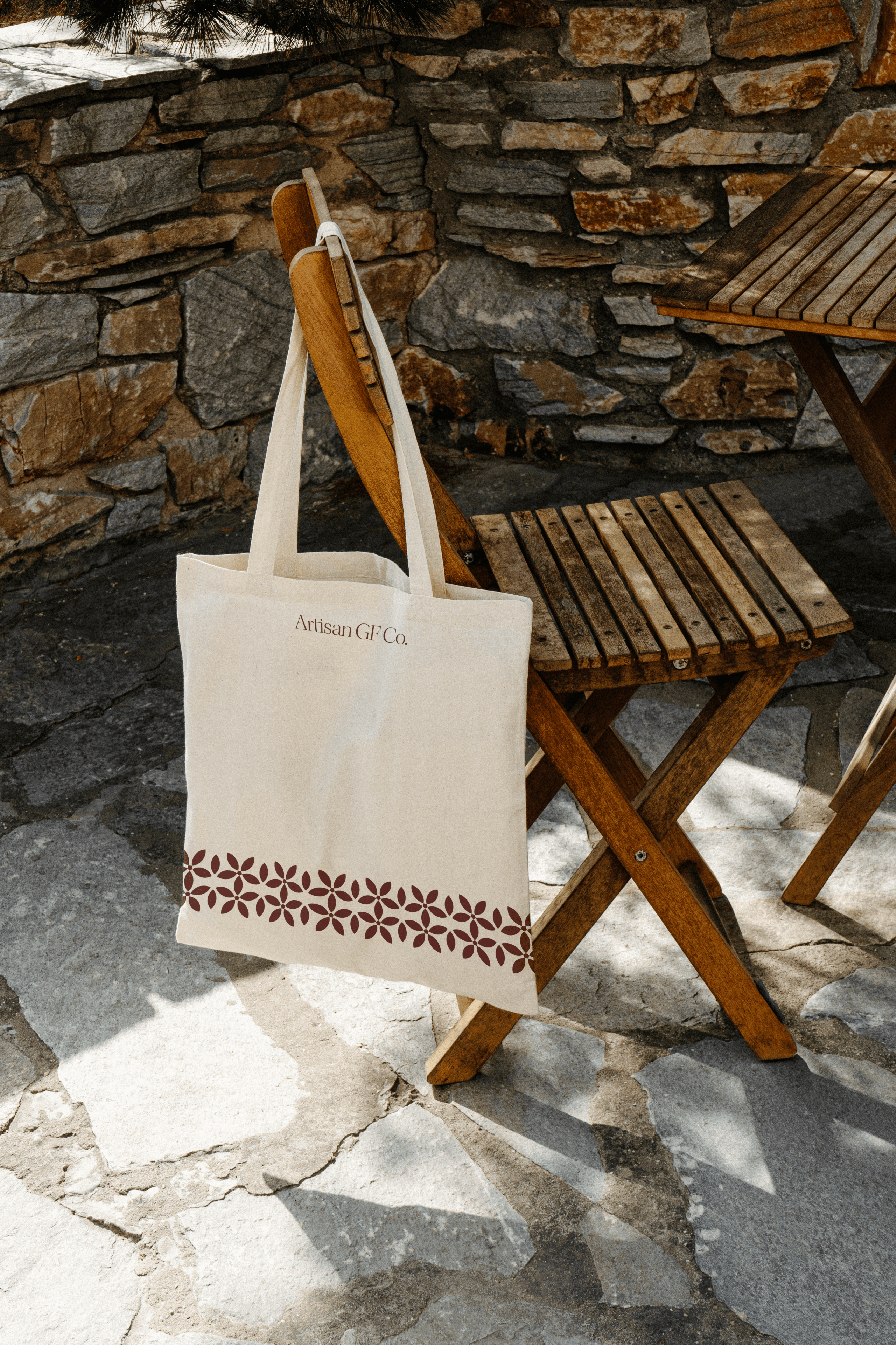Artisan GF Co. tote bag hanging from a timber chair against a stone wall